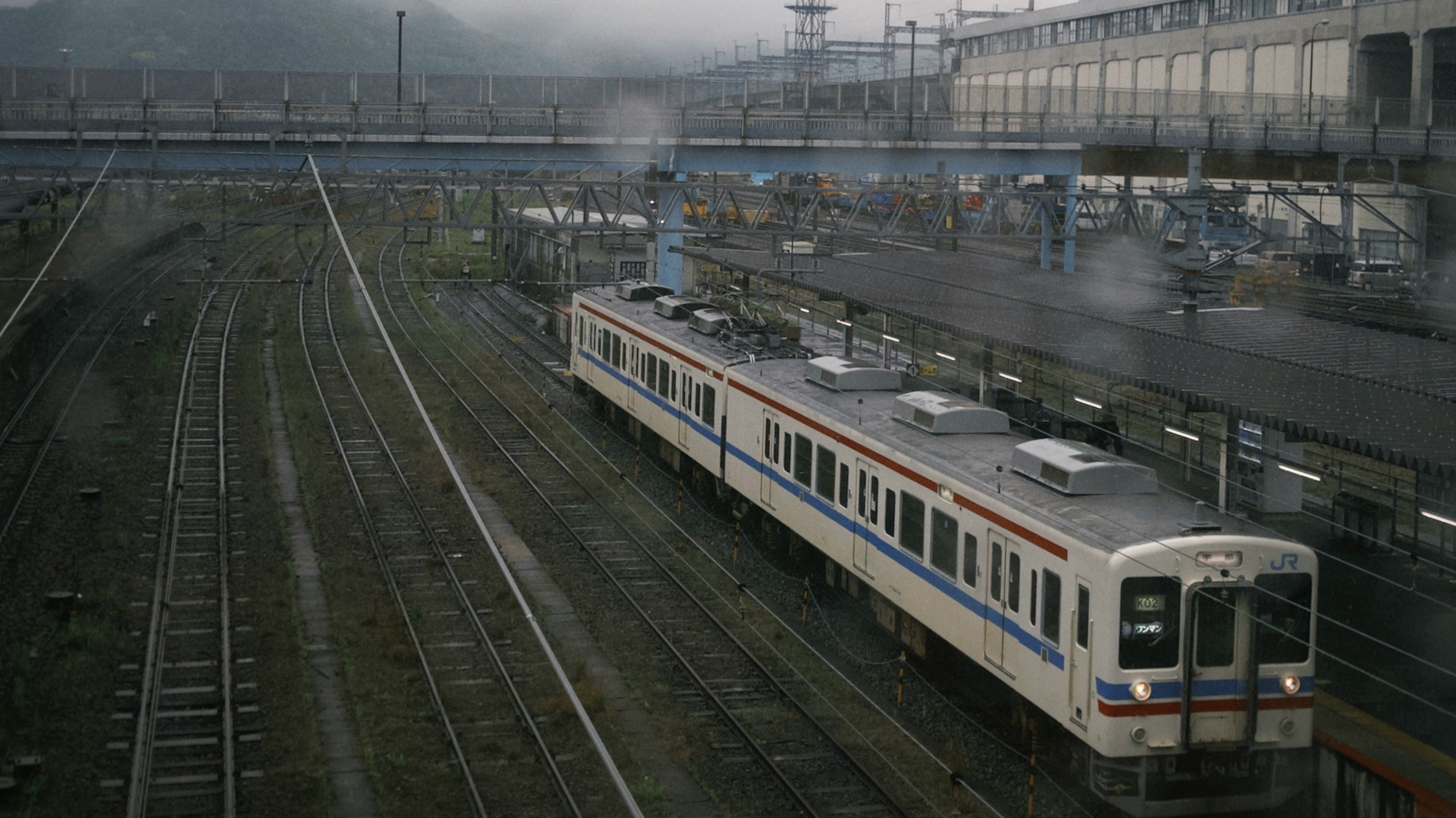 霧の中を走る列車が線路沿いに並ぶ車両基地の風景