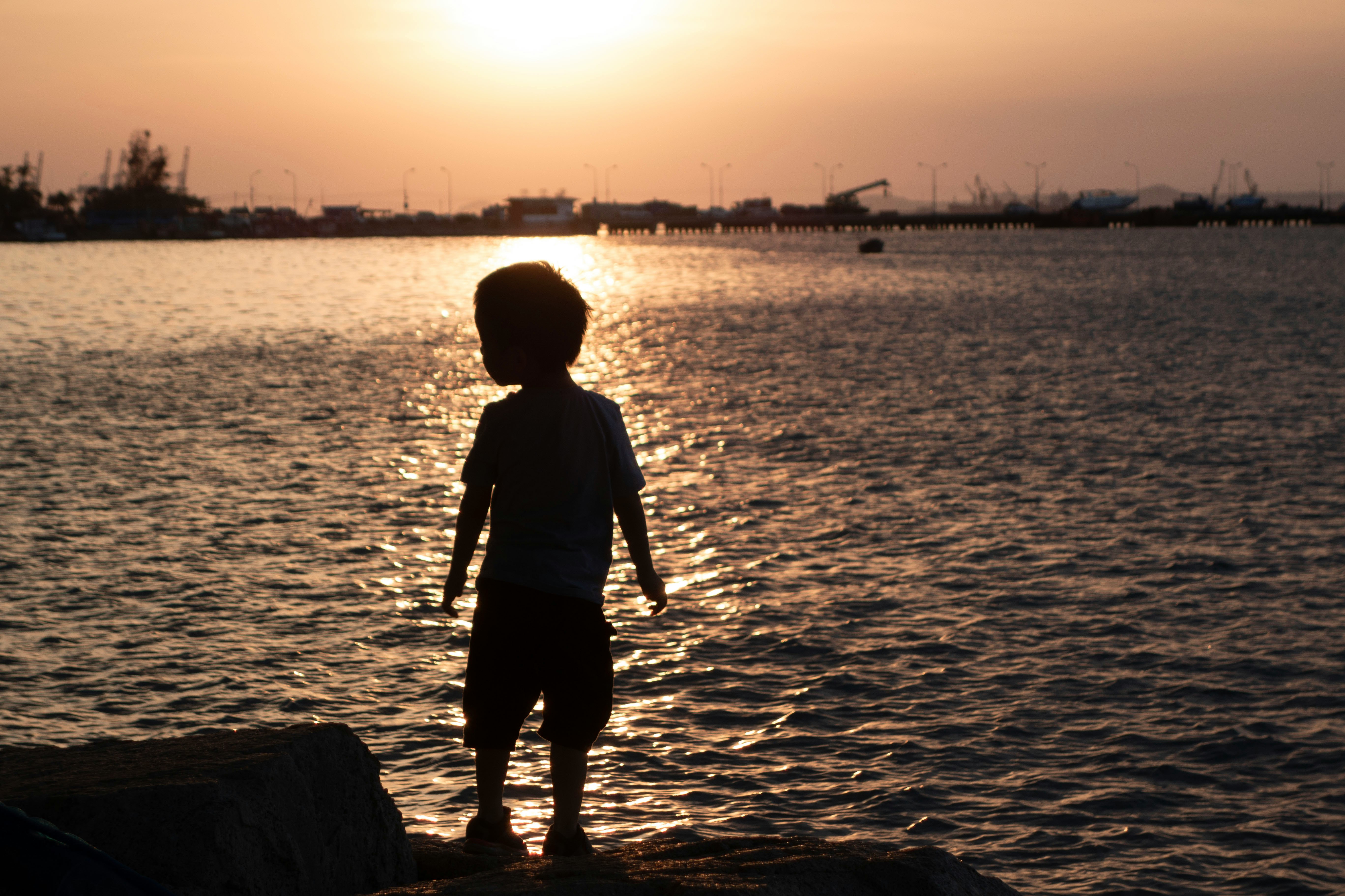 夕日に照らされた海辺で立つ子どものシルエット