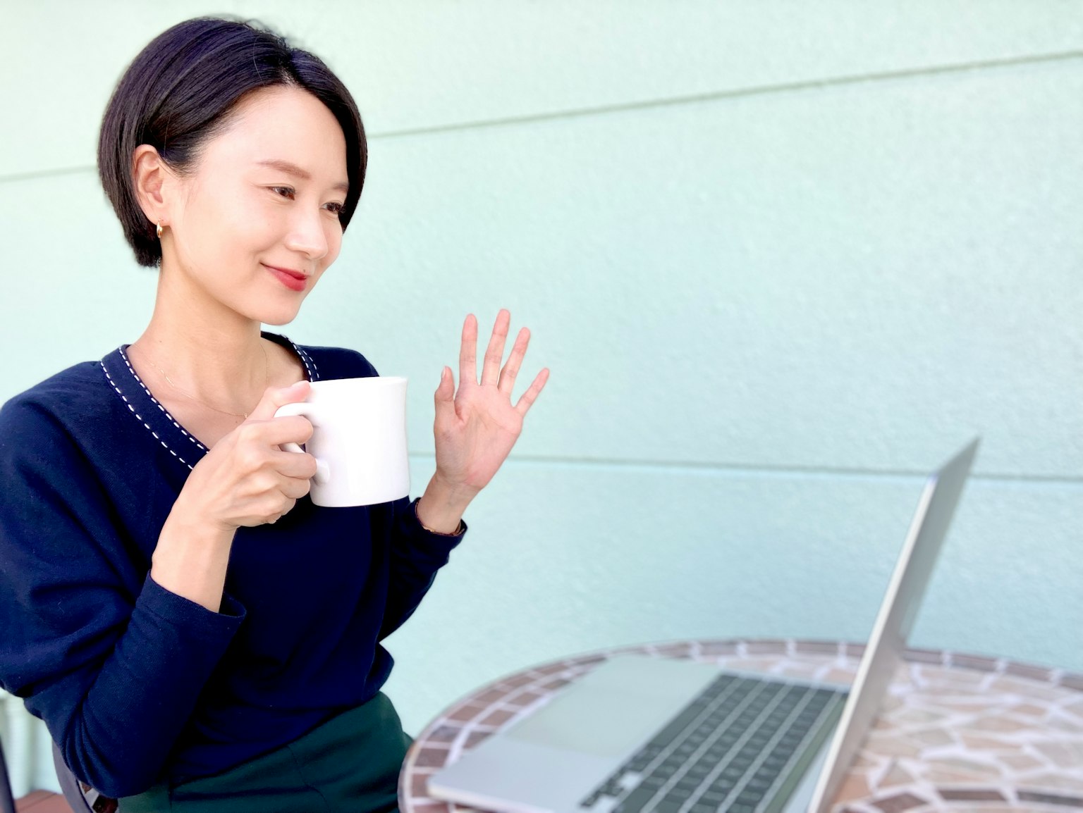 Woman smiling while holding a coffee cup in front of a laptop