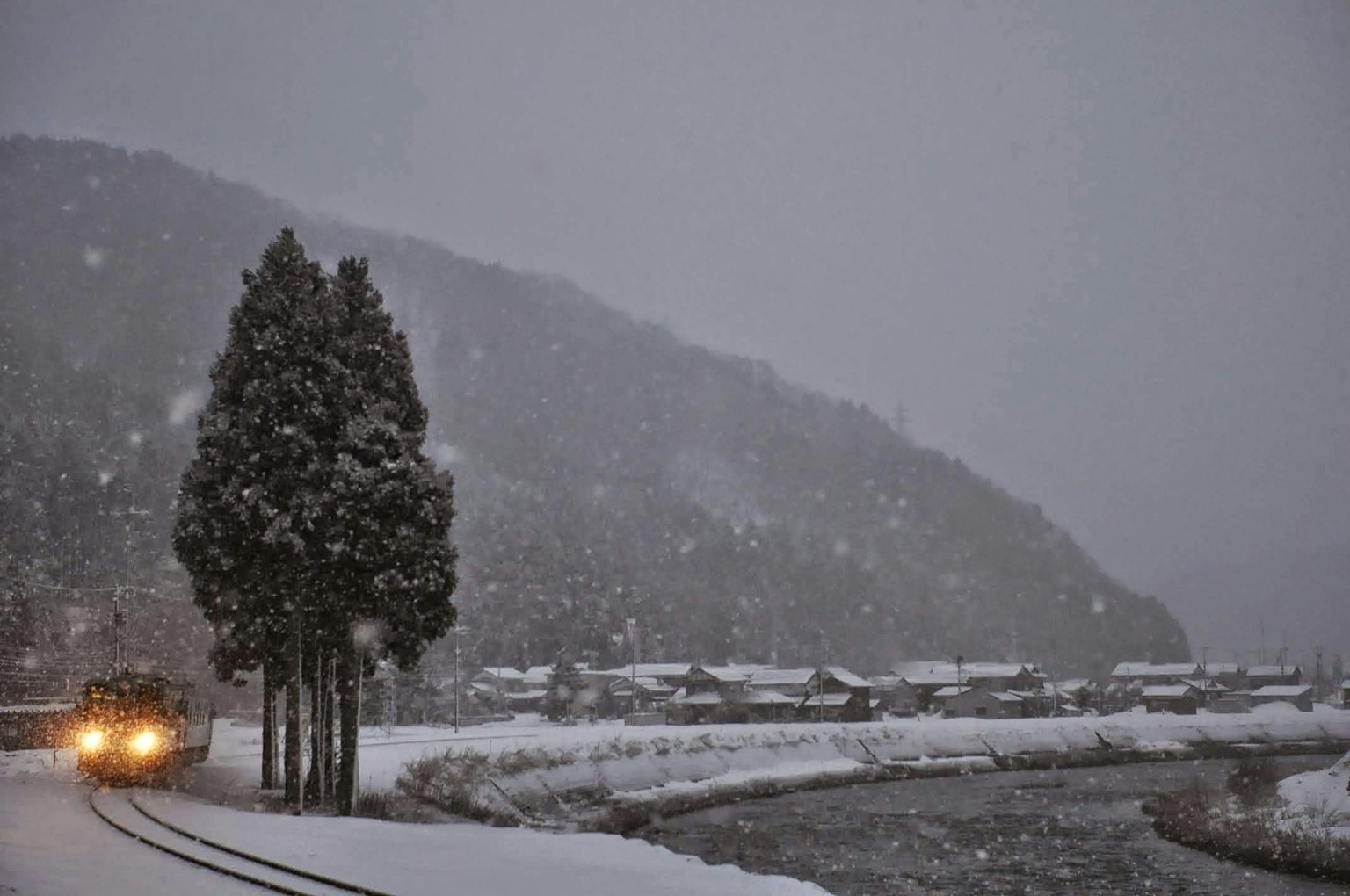 Train traveling along a snow-covered landscape with trees and a river
