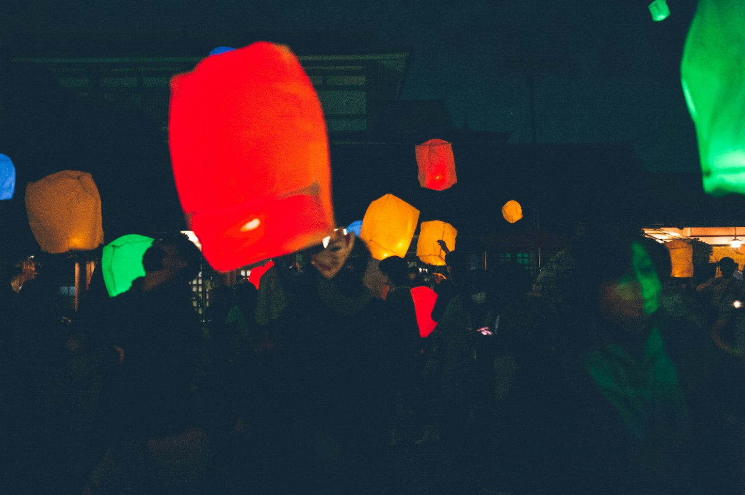 Colorful lanterns floating in the night sky with silhouettes of people