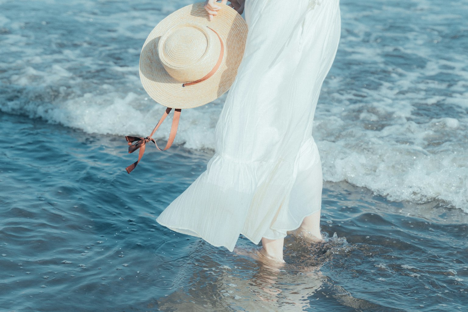 海灘上穿著白色連衣裙的女人手持帽子