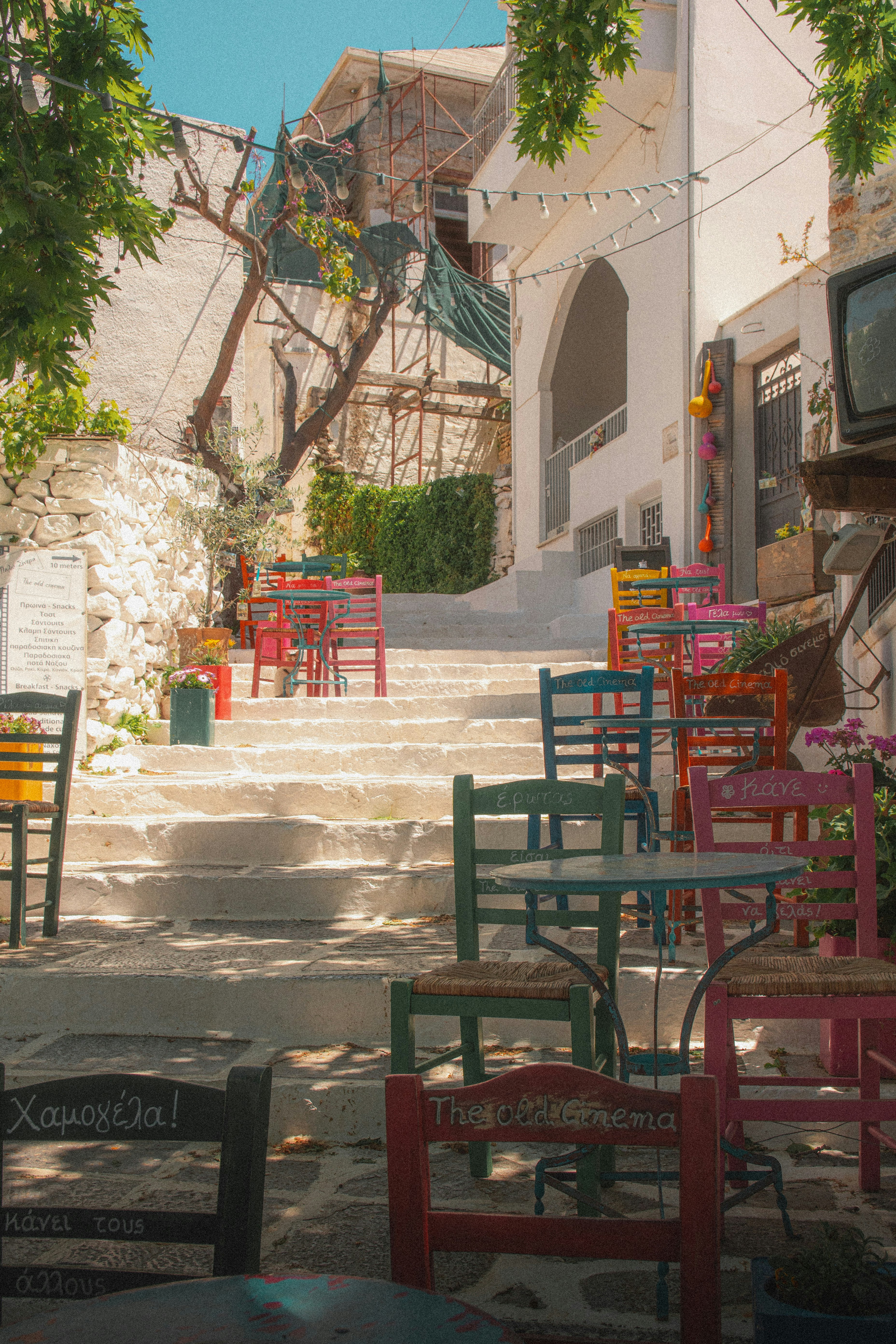 Entrée de café dans une ruelle, avec chaises et tables colorées près d’un escalier