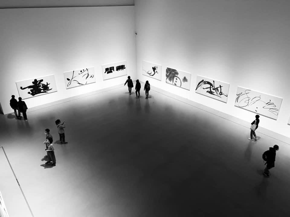白い壁に展示されたモノクロのアートと人がいる美術館の展示室