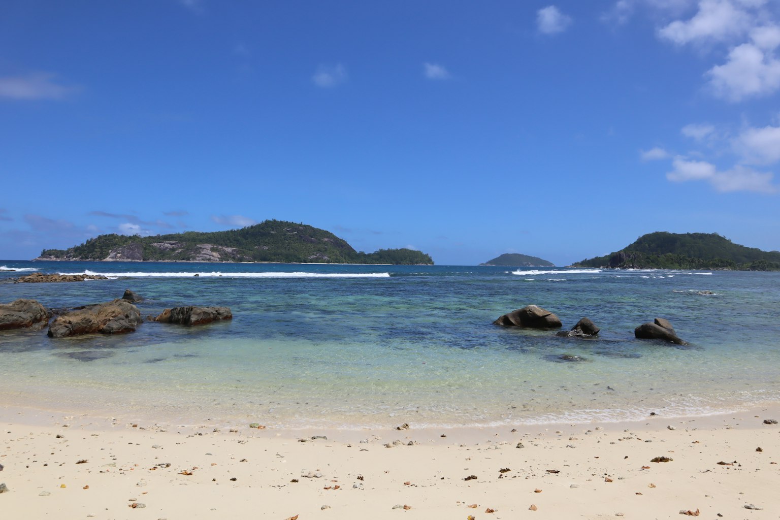 Scenic view of blue sky and ocean with white sandy beach and rocks in foreground