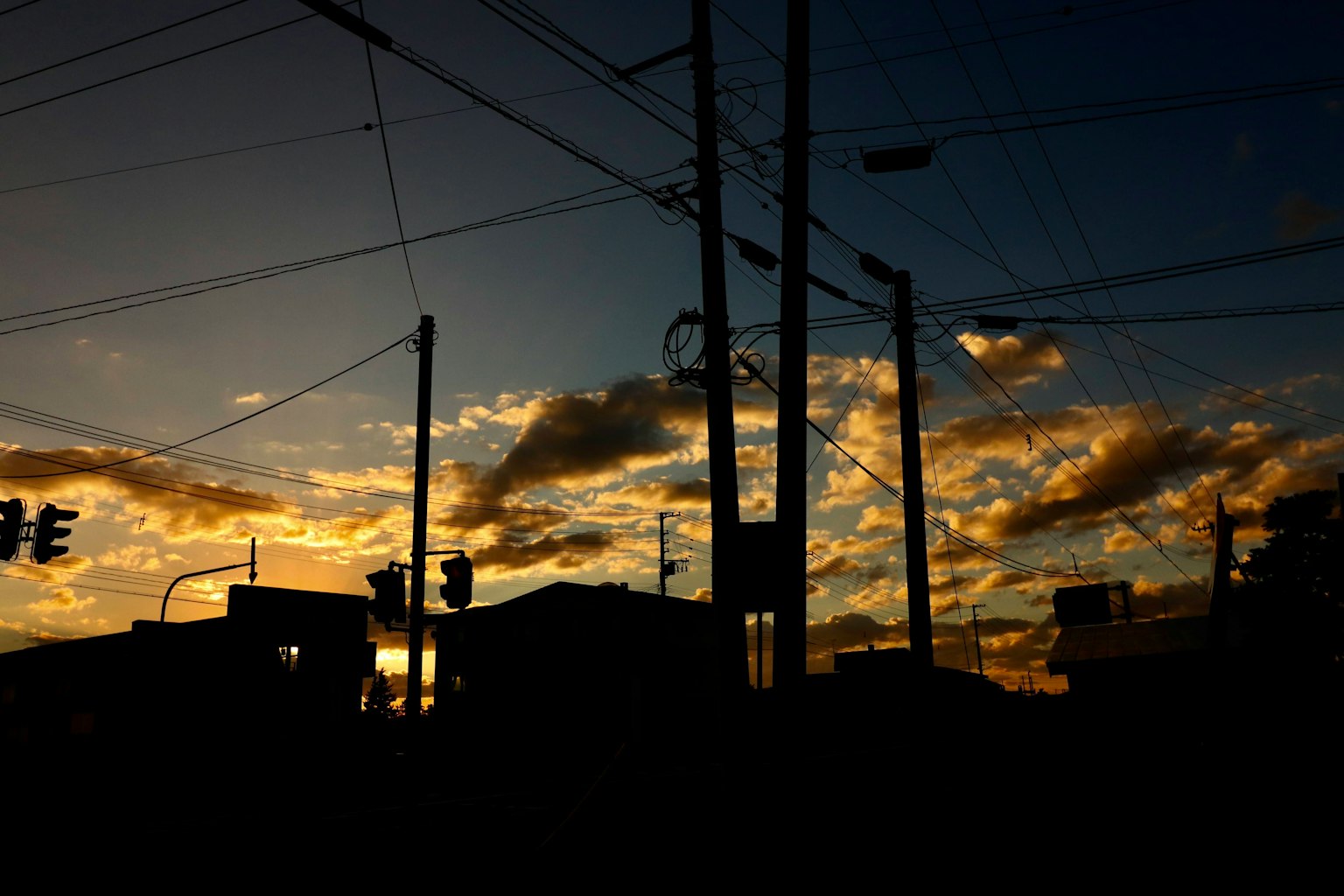 Silueta de edificios y líneas eléctricas contra un cielo de atardecer con nubes