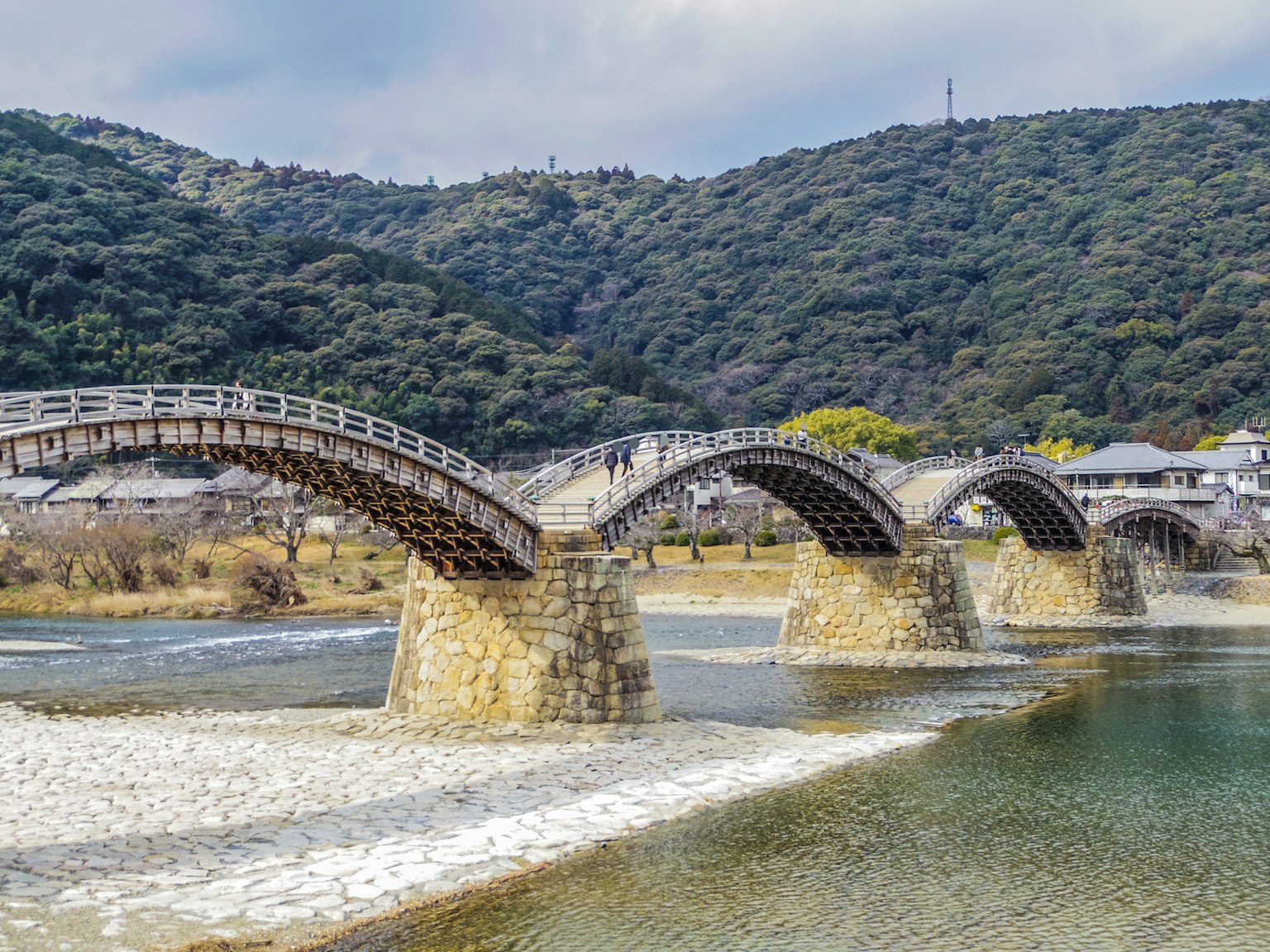 Eine schöne Holzbogenbrücke überspannt einen Fluss, umgeben von grünen Bergen