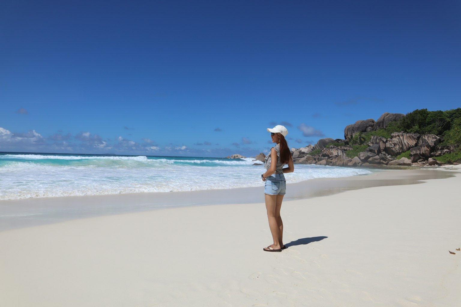 Une femme debout sur une plage de sable blanc avec des vagues océaniques bleues