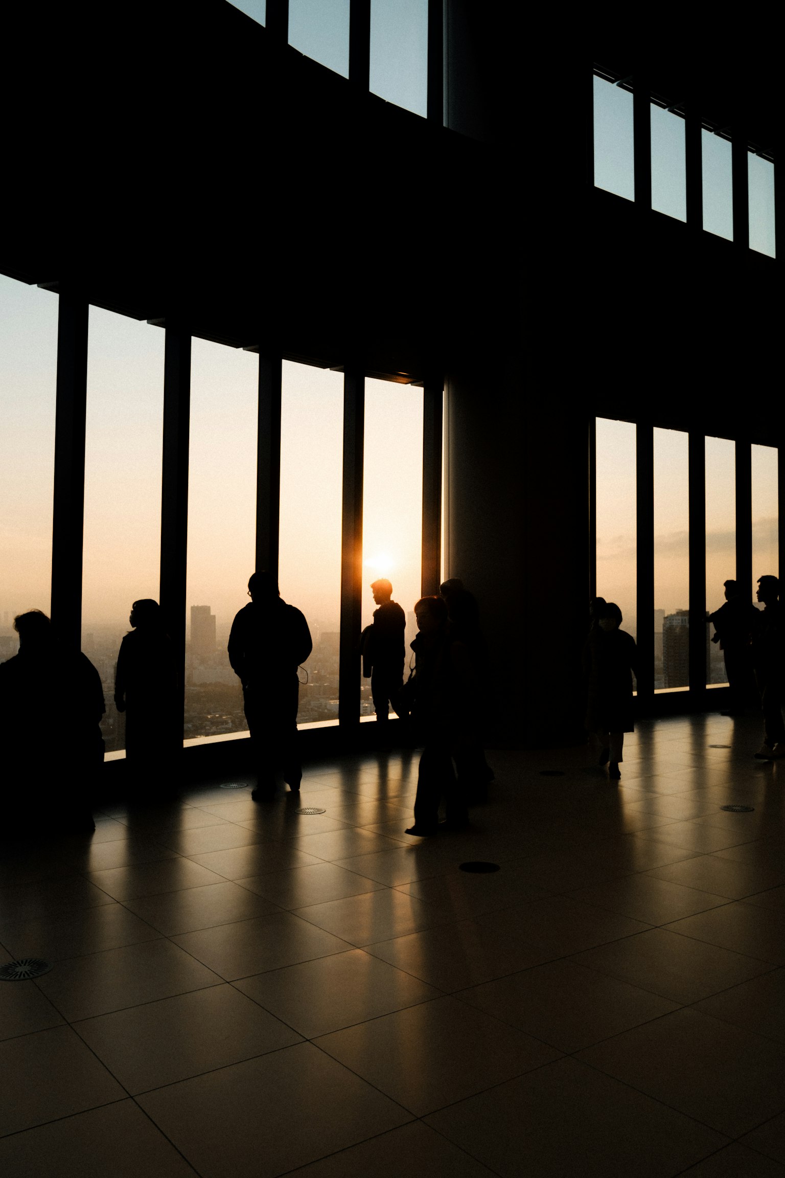 Personas de pie junto a grandes ventanas mirando el atardecer