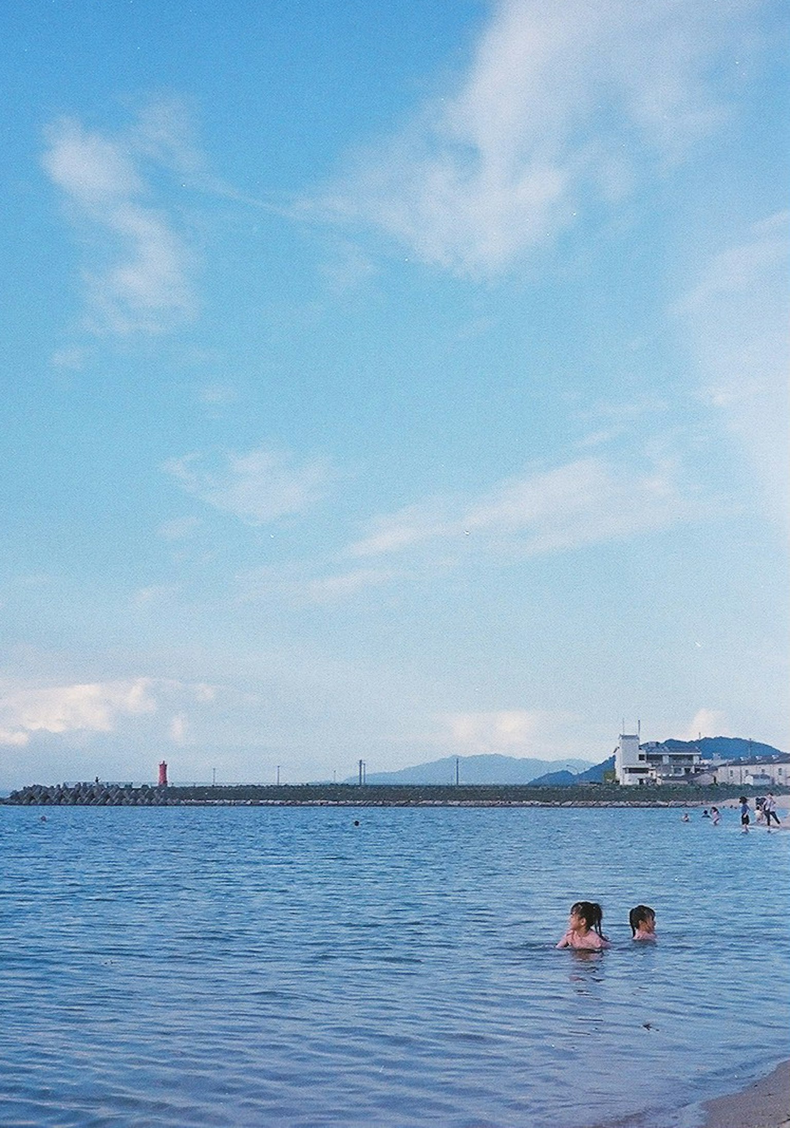Zwei Kinder spielen im ruhigen Wasser unter einem blauen Himmel