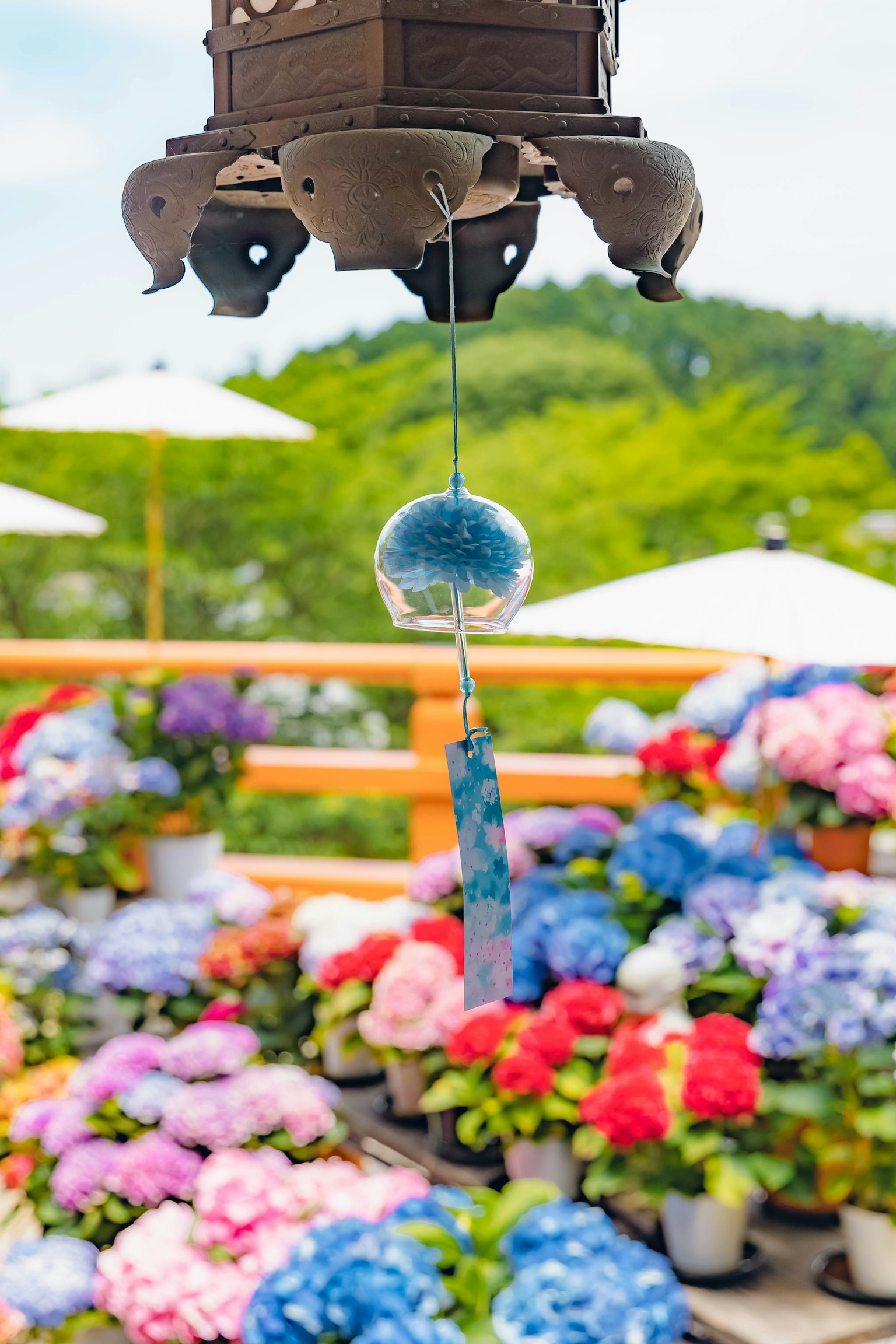A blue wind chime hanging in front of colorful flowers