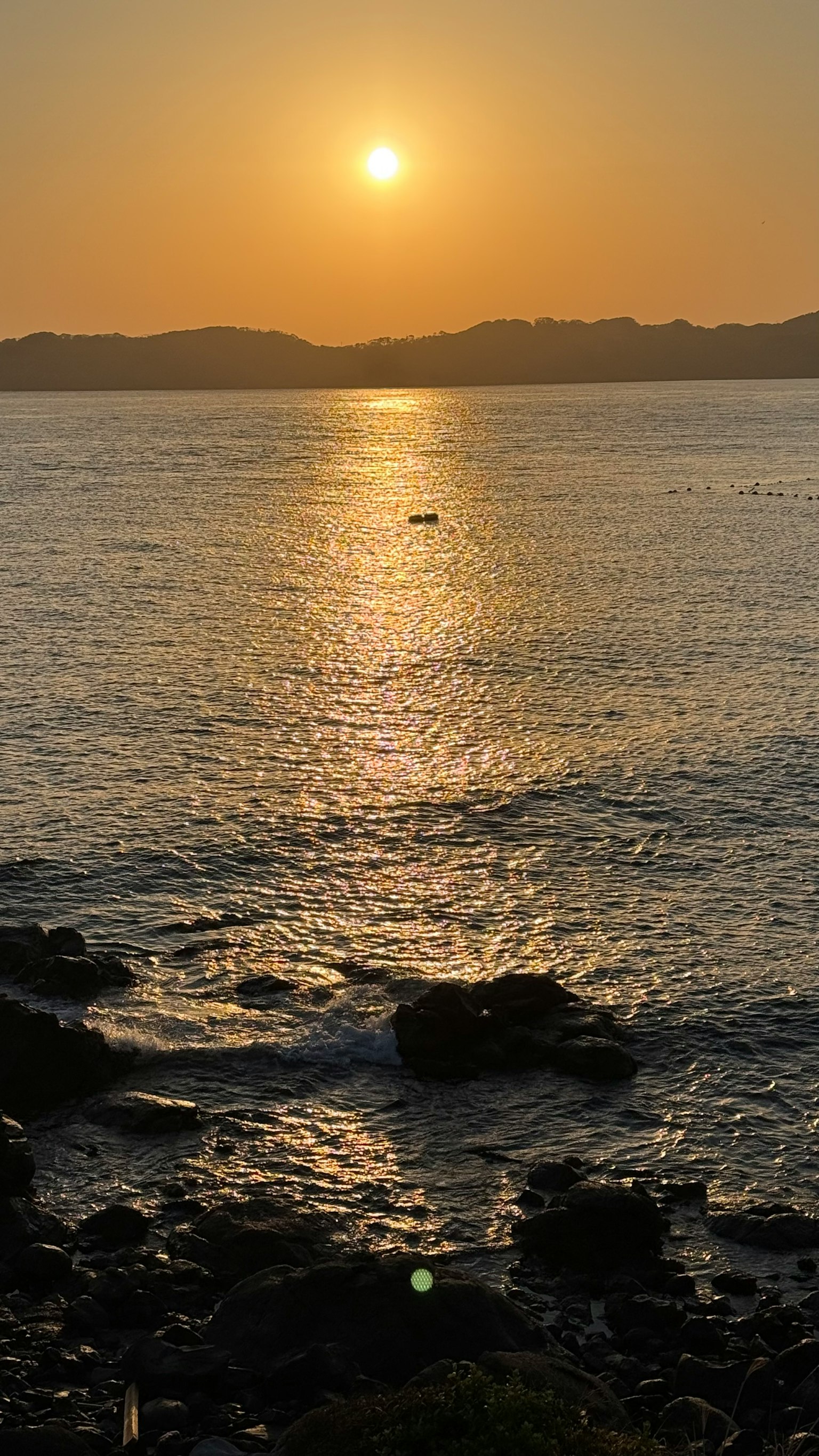 Beautiful sunset reflecting on the ocean with rocky shoreline and gentle waves