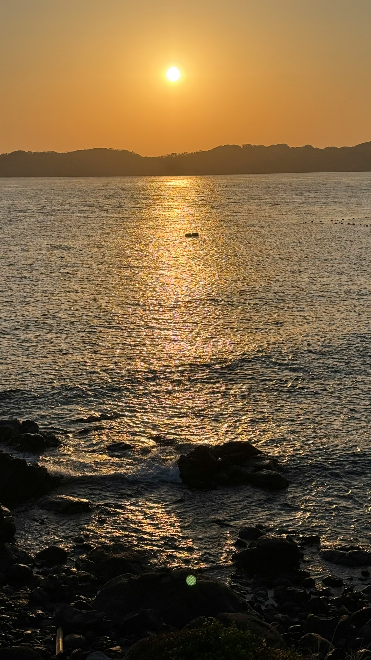 Pemandangan matahari terbenam yang indah memantulkan lautan dengan garis pantai berbatu dan gelombang lembut