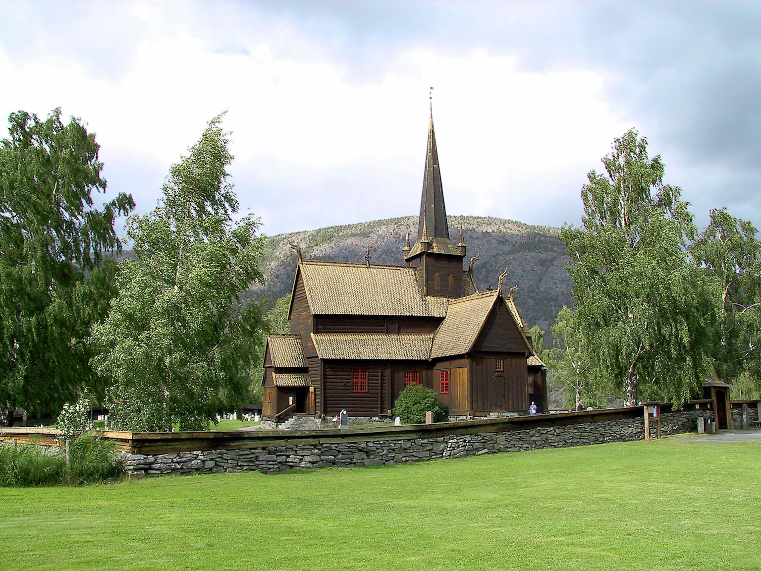 Rote Holzkirche auf grünem Gras mit Bergen im Hintergrund