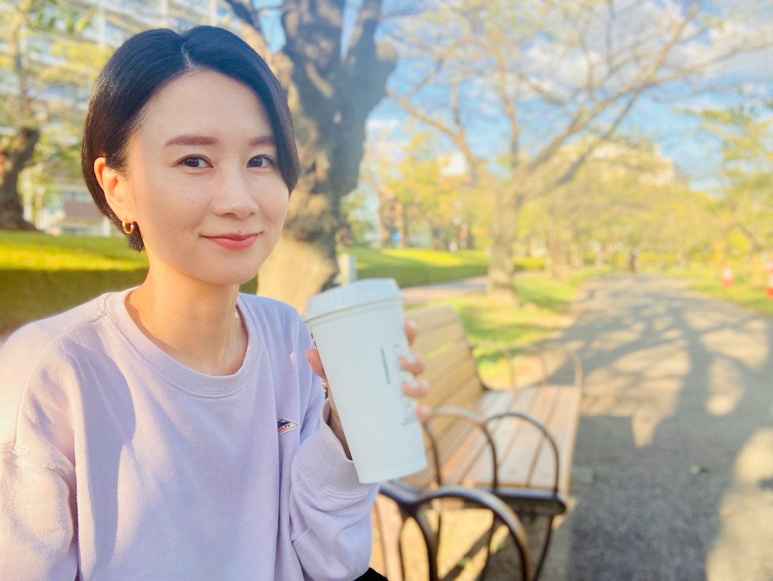 공원에서 흰색 컵을 들고 있는 웃고 있는 여성