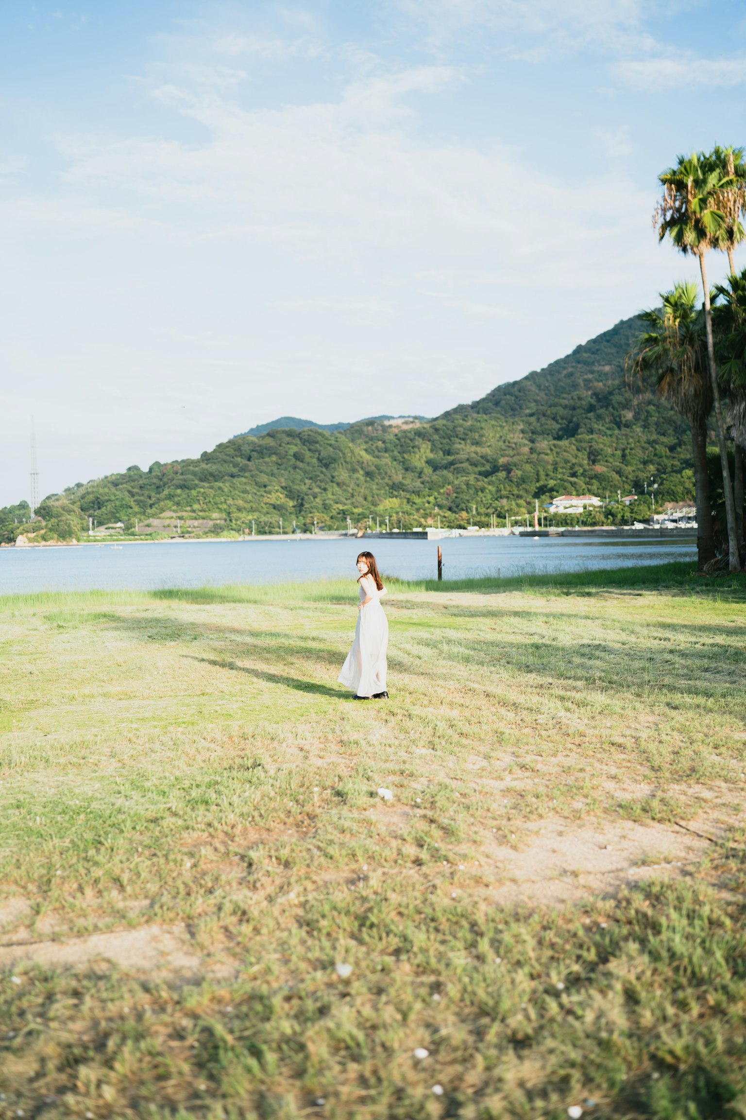 A woman standing on a wide grassy area with a blue sky and mountains in the background