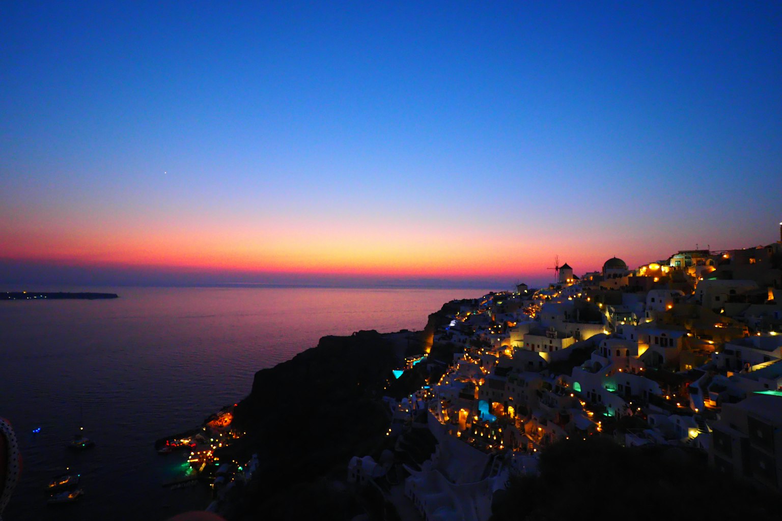 Magnifique vue du coucher de soleil sur l'île de Santorin avec un ciel dégradé et des lumières scintillantes