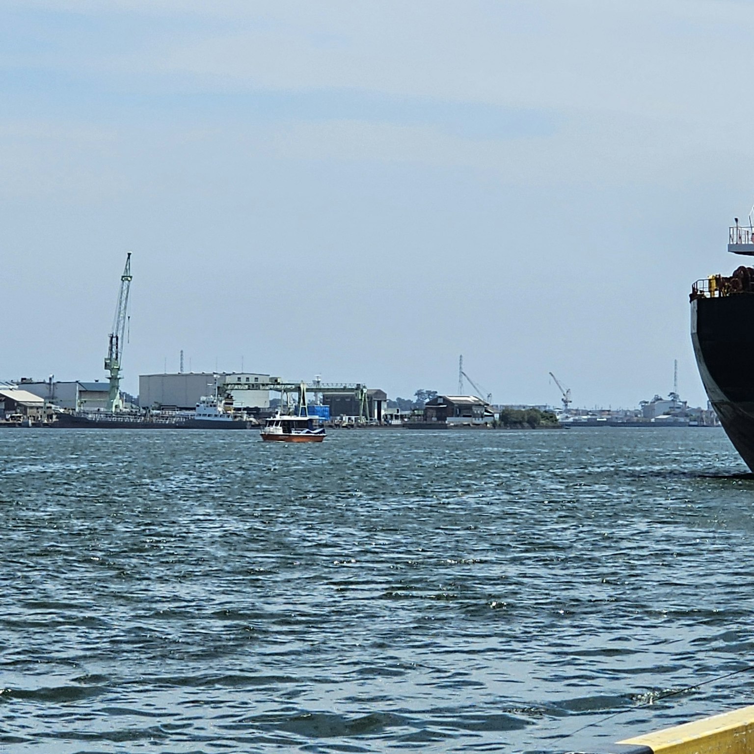 Un grand navire et un petit bateau sur l'eau avec un port en arrière-plan