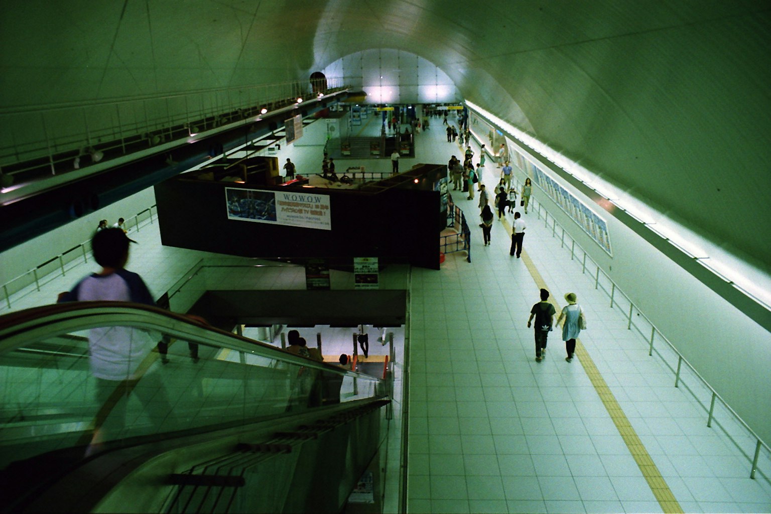 Amplio pasillo de estación de metro con escalera mecánica y peatones visibles