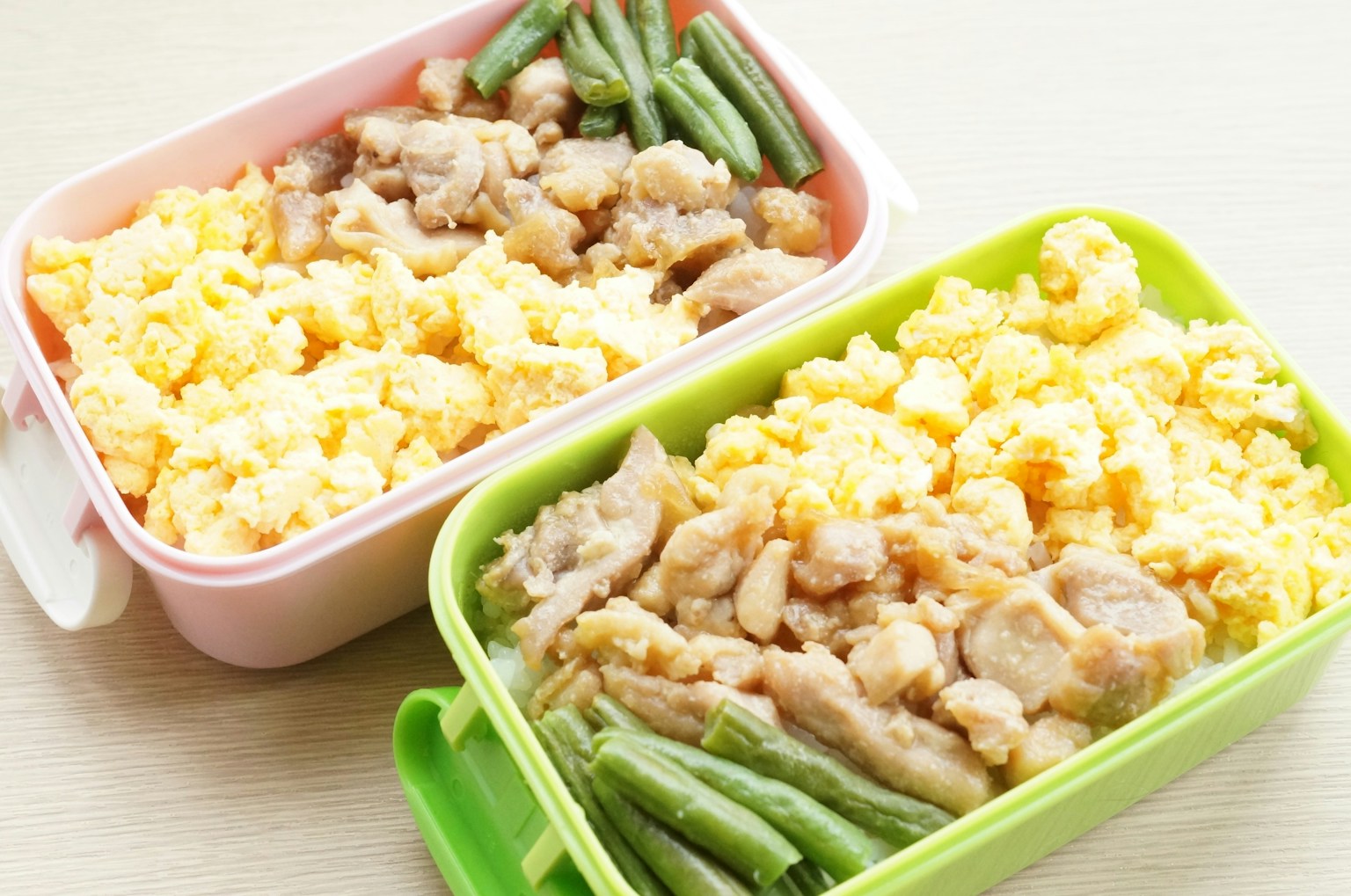 二つの弁当箱に盛られた鶏肉、卵、インゲン