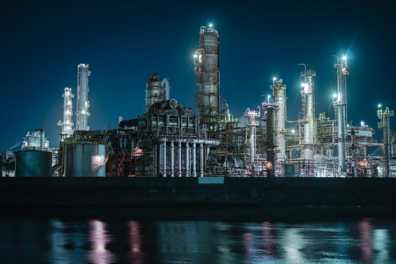 Industrielandschaft bei Nacht mit Fabrikschornsteinen und hellen Lichtern