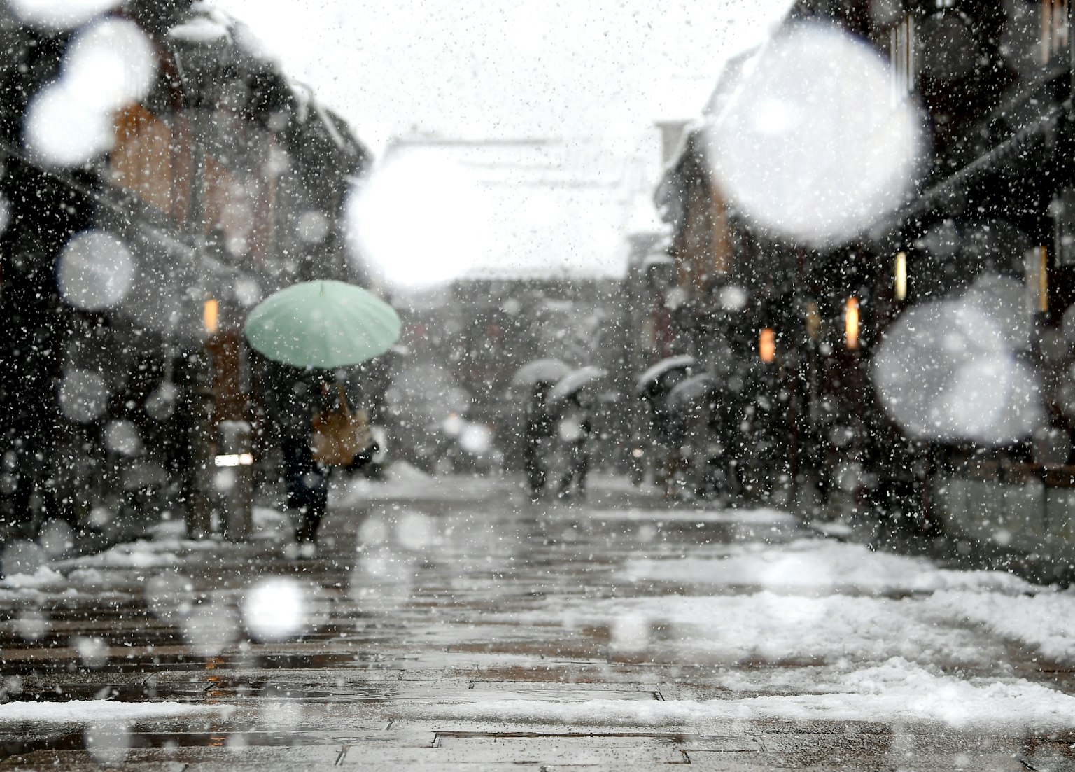 Verschneite Straßenszene mit Menschen, die Regenschirme tragen