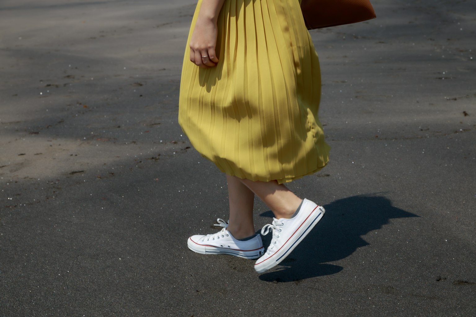 Una donna in abito giallo che cammina con scarpe da ginnastica bianche