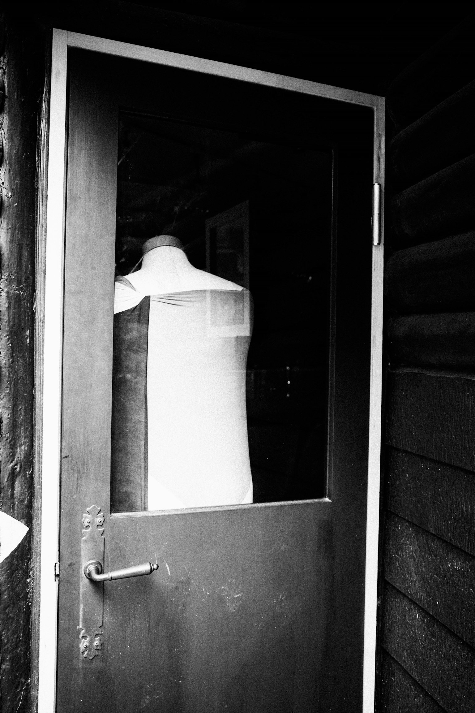 White mannequin visible through a glass door in black and white