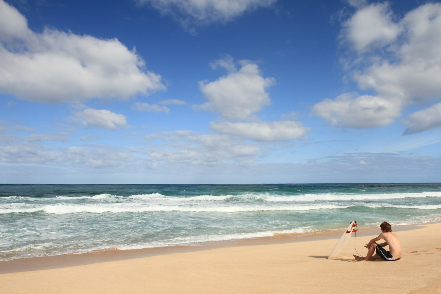 Dos personas sentadas en una playa de arena bajo un cielo azul