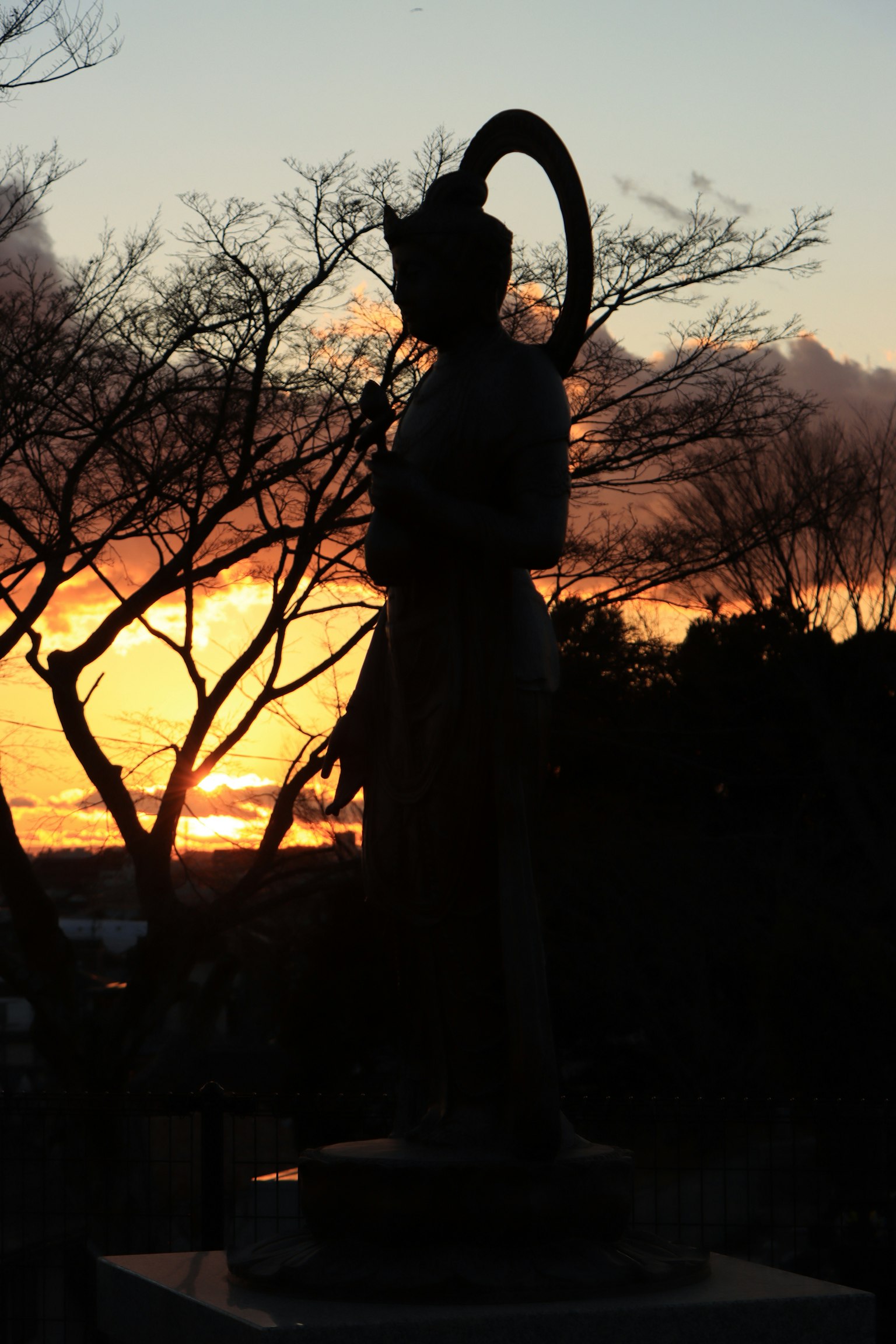 Silhouette of a statue against a sunset with trees in the background