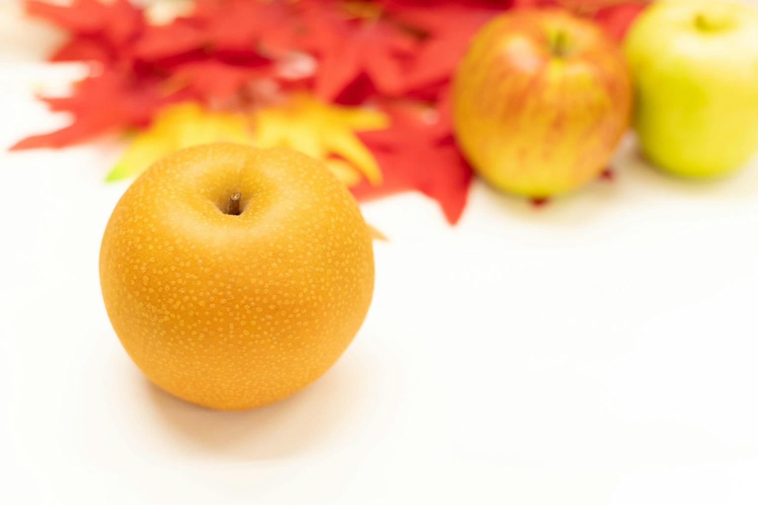 Une poire orange au premier plan avec des feuilles rouges et des pommes en arrière-plan