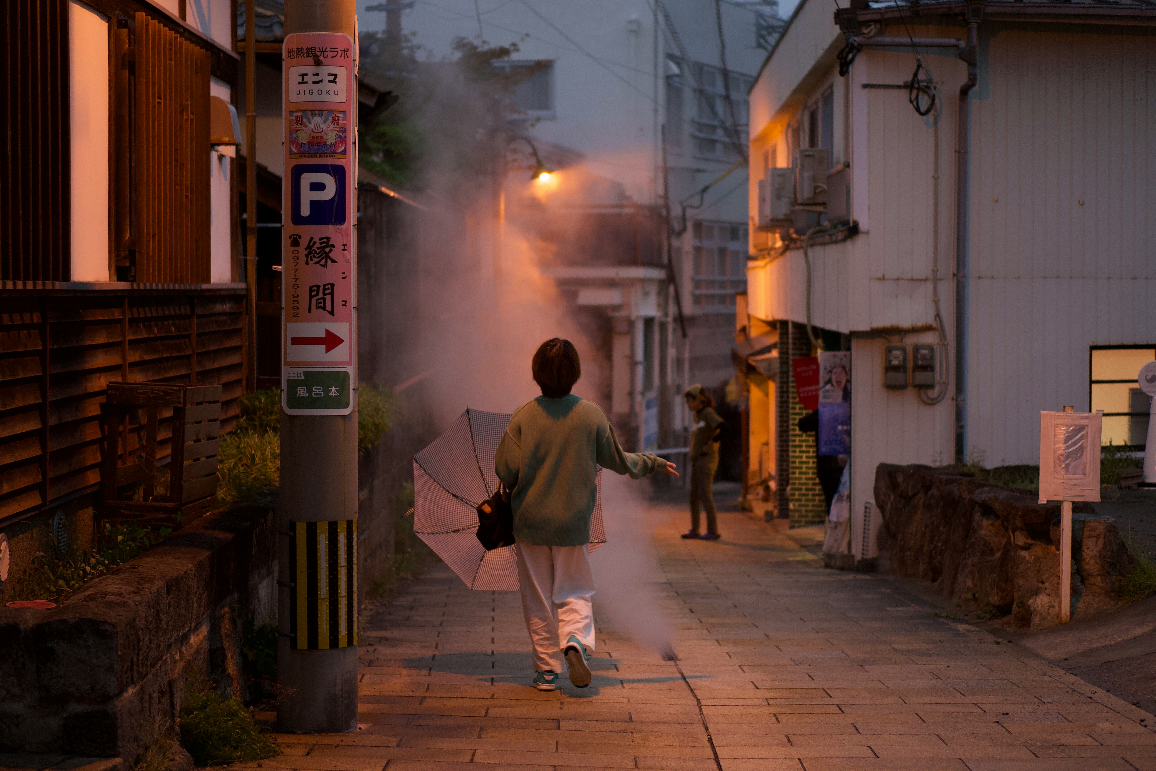 路地の夕暮れに立つ人物と煙の漂う商店街の通り