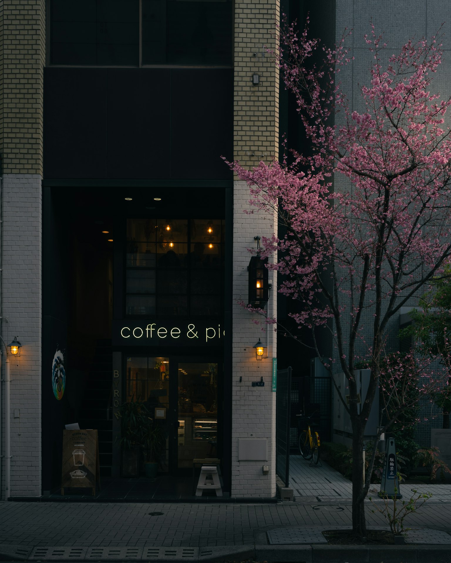 Façade d'un café avec un arbre en fleurs roses et une enseigne pour café et pizza