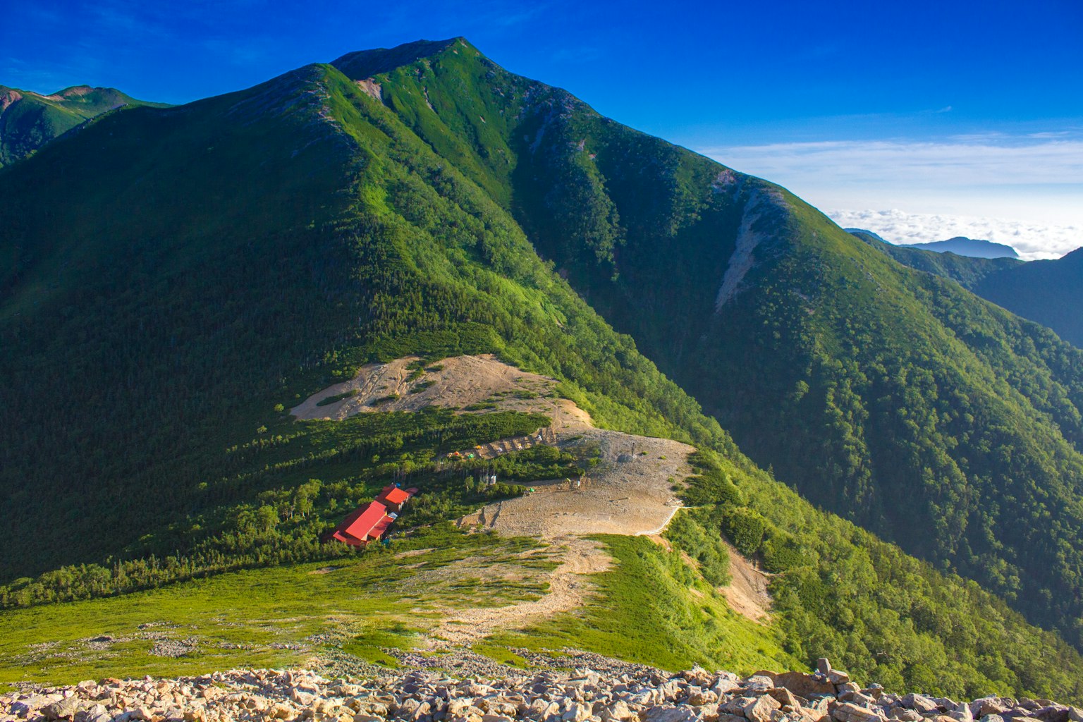 Vue panoramique de montagnes vertes avec une cabane rouge sous un ciel bleu