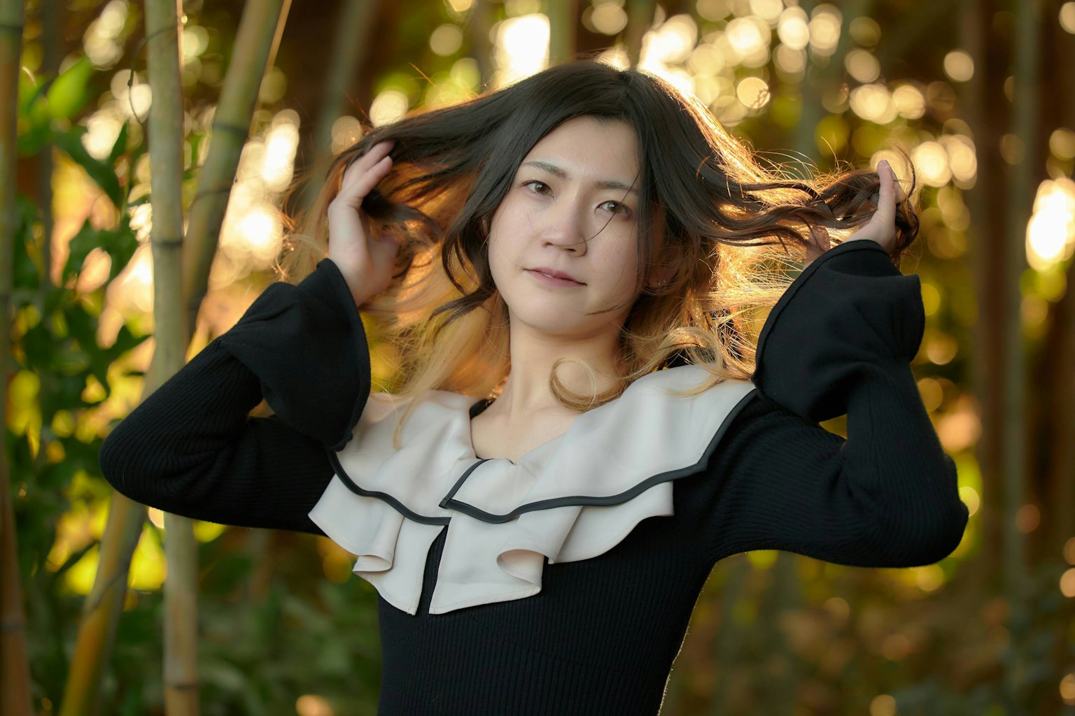 Portrait of a woman lifting her hair with a blurred bamboo background