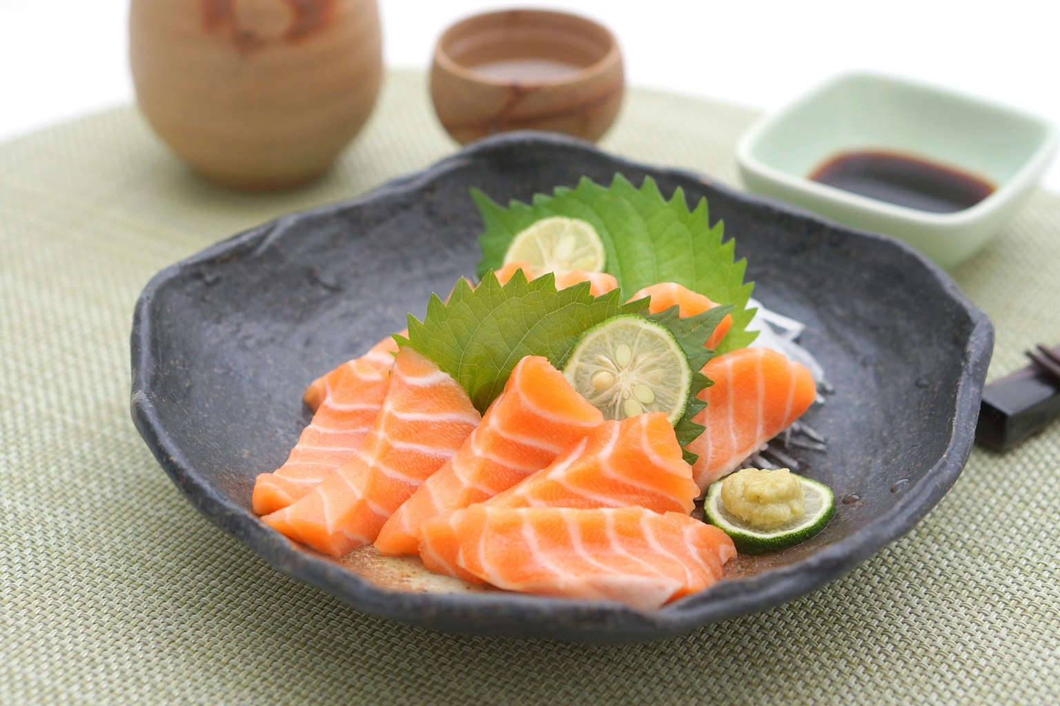 Sashimi de saumon frais présenté sur une assiette noire avec des tranches de citron vert