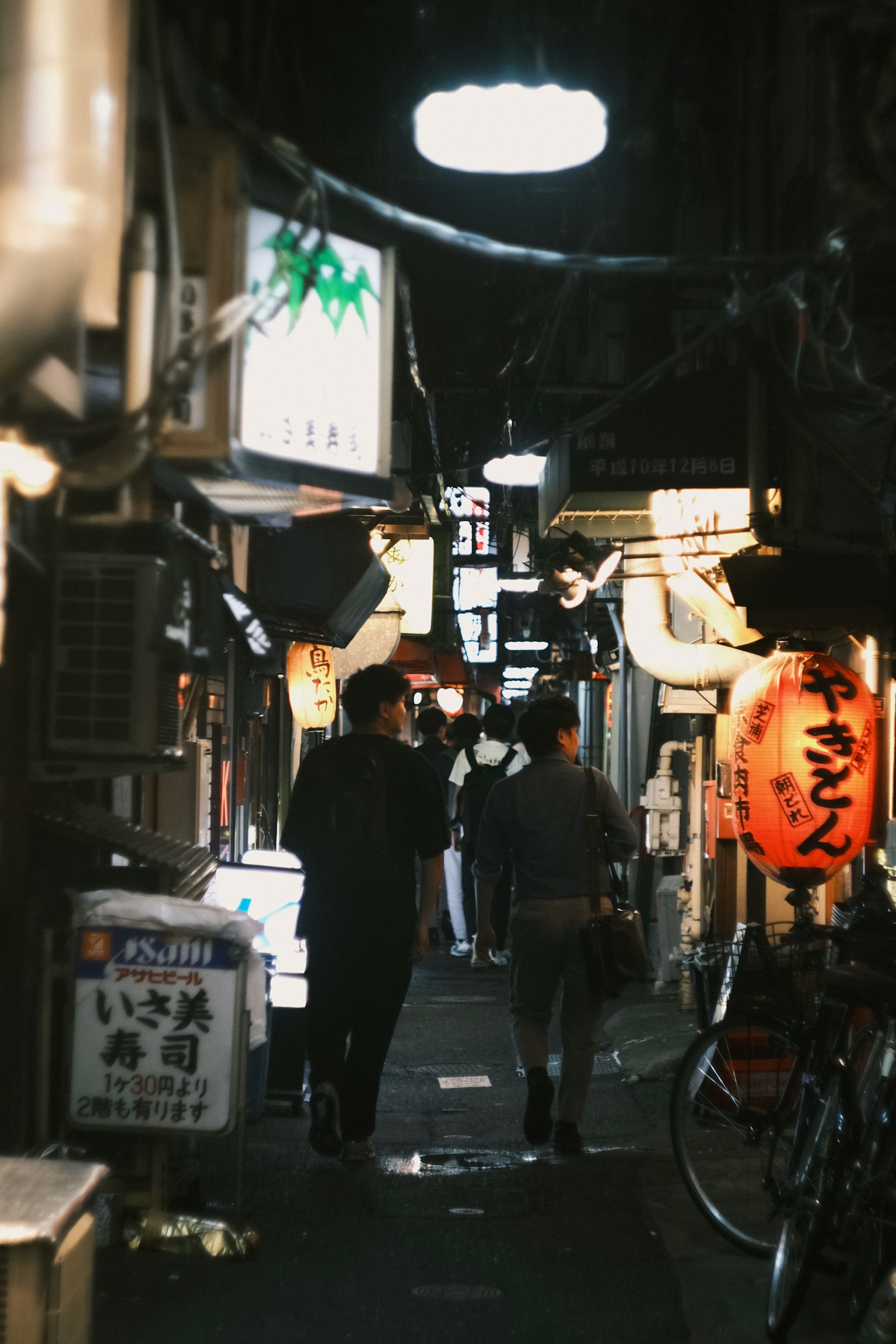 狭い路地に人々が歩いている夜の風景 明かりが灯る看板と自転車が見える