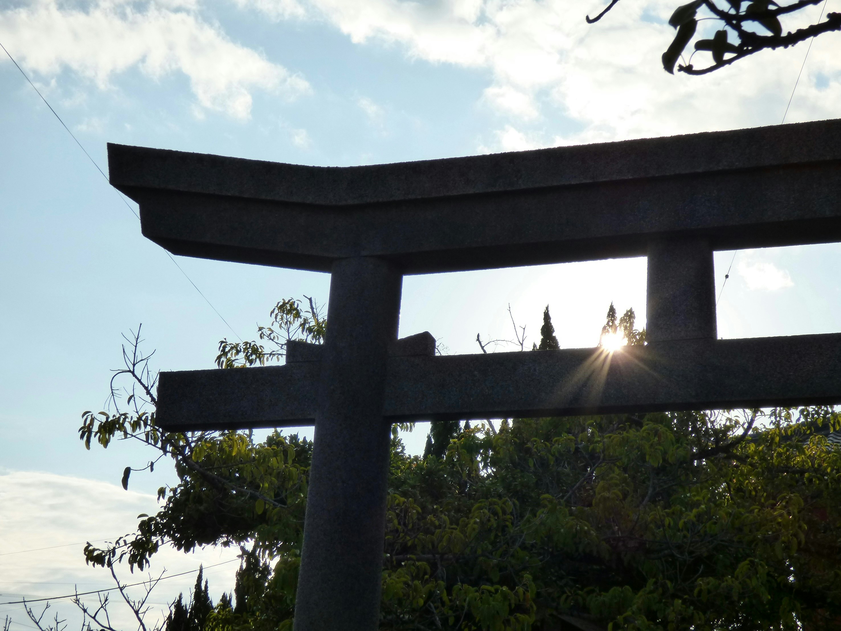 鳥居のシルエットと背後の太陽の光が見える風景