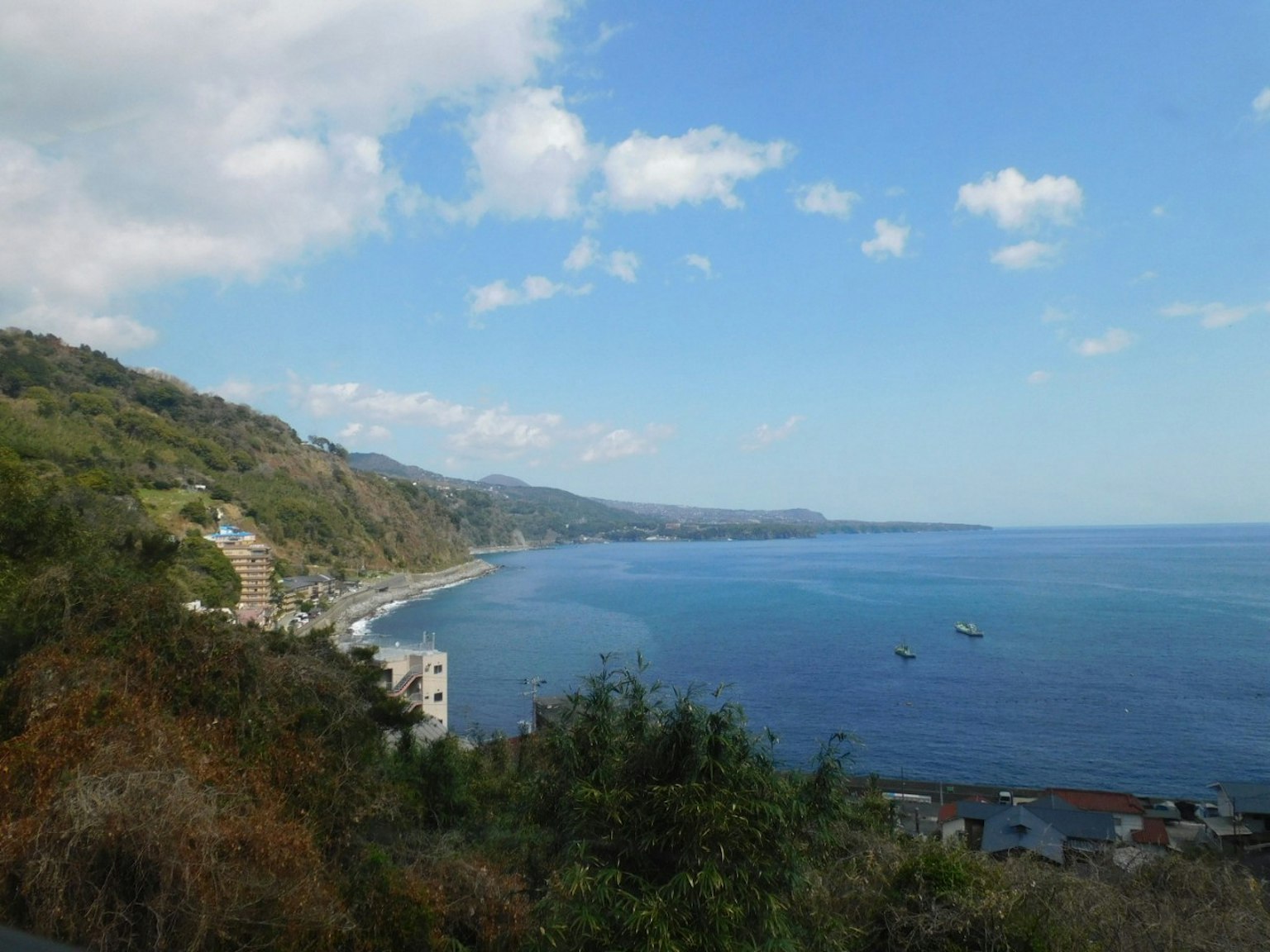 Pemandangan laut biru dan bukit hijau di bawah langit yang sebagian mendung