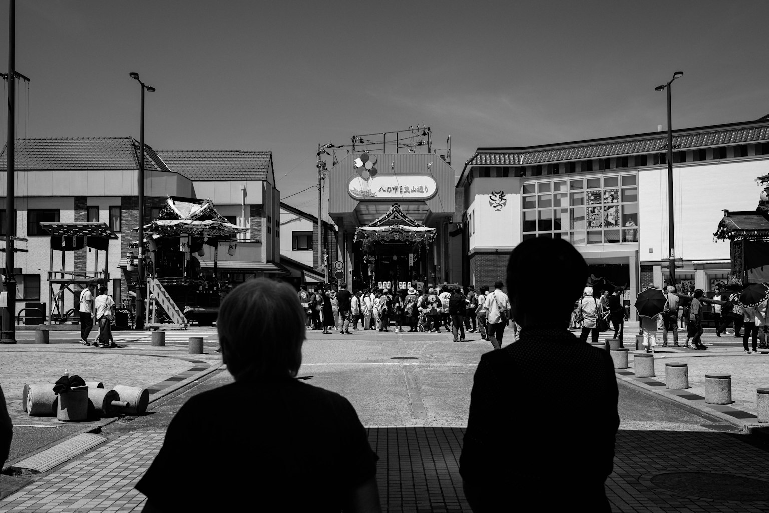 Silhouettes of two people observing a bustling square in black and white