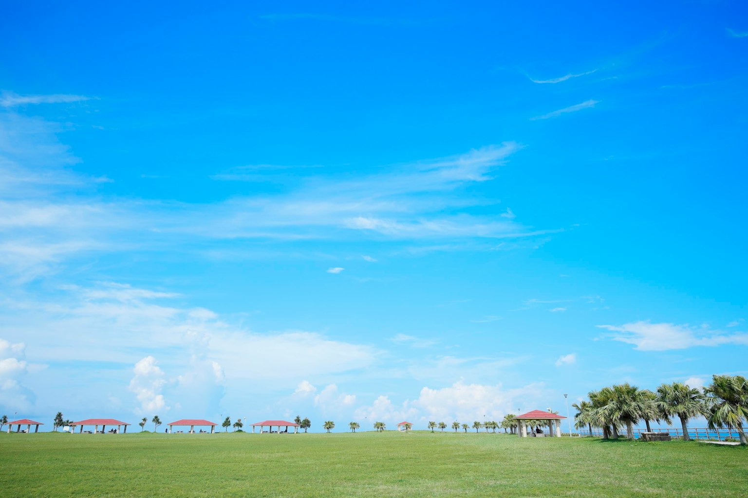 青空と緑の草原に赤い屋根のパビリオンが並ぶ風景