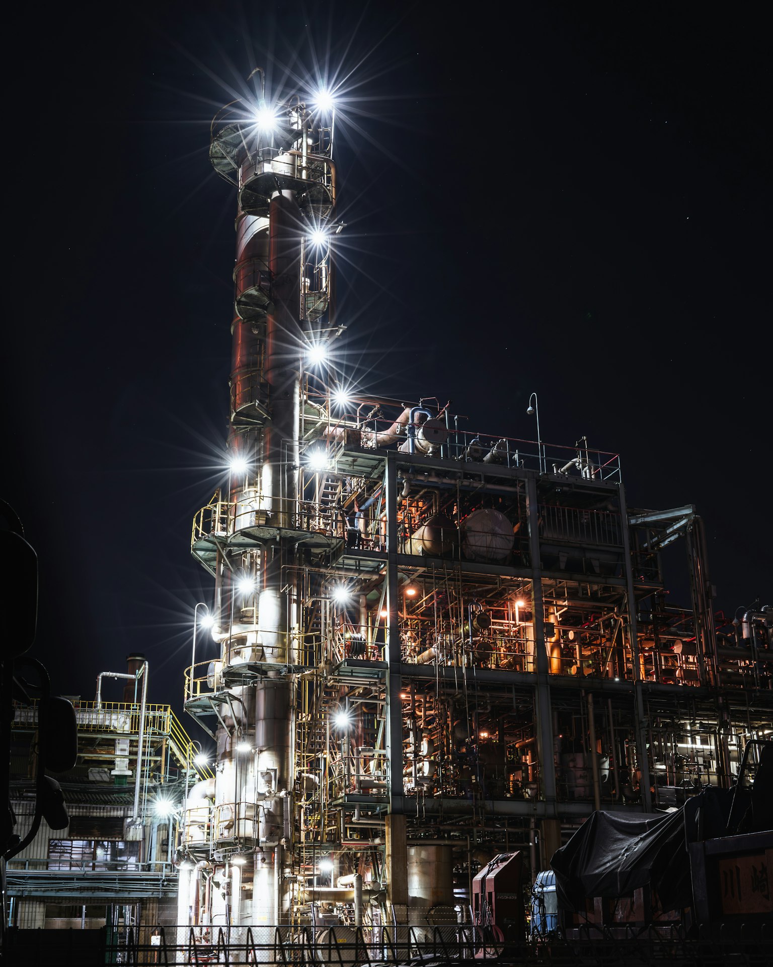 Industrielle Anlage bei Nacht beleuchtet mit hellen Lichtern und einem hohen Schornstein