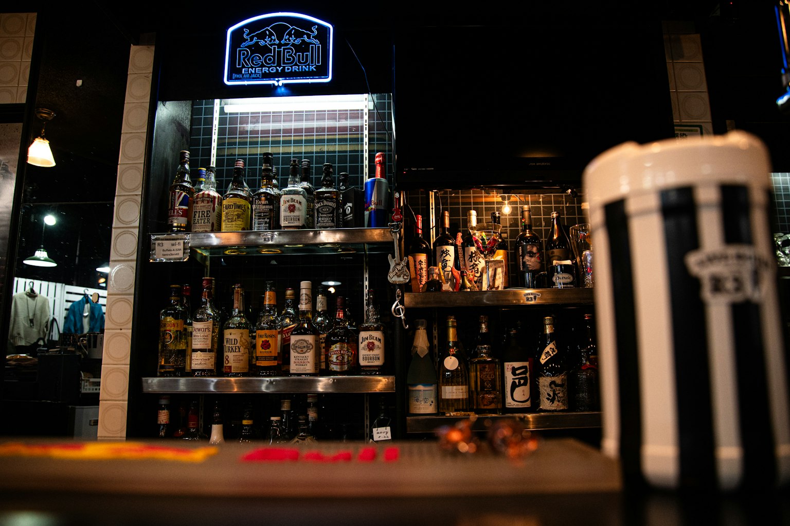 Interior de un bar con varias botellas de licor en estantes y una jarra de cerveza a rayas en primer plano