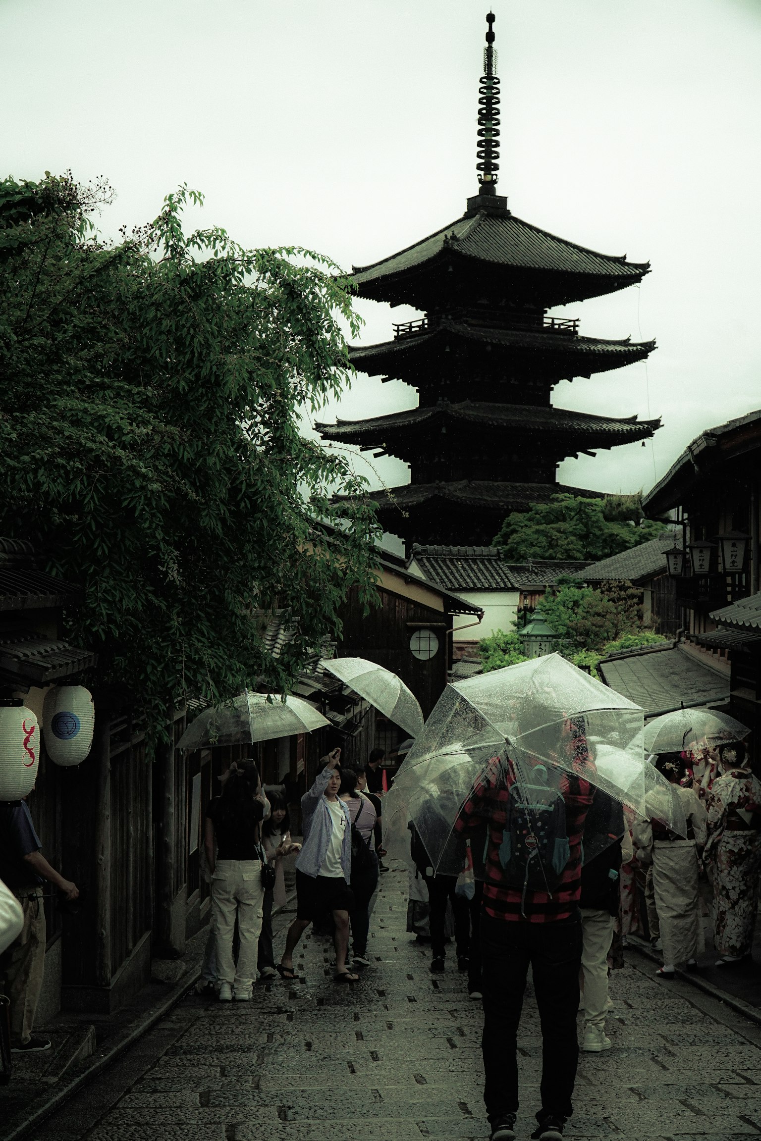 Des touristes marchant sous des parapluies dans une rue de Kyoto avec une pagode en arrière-plan par un jour de pluie