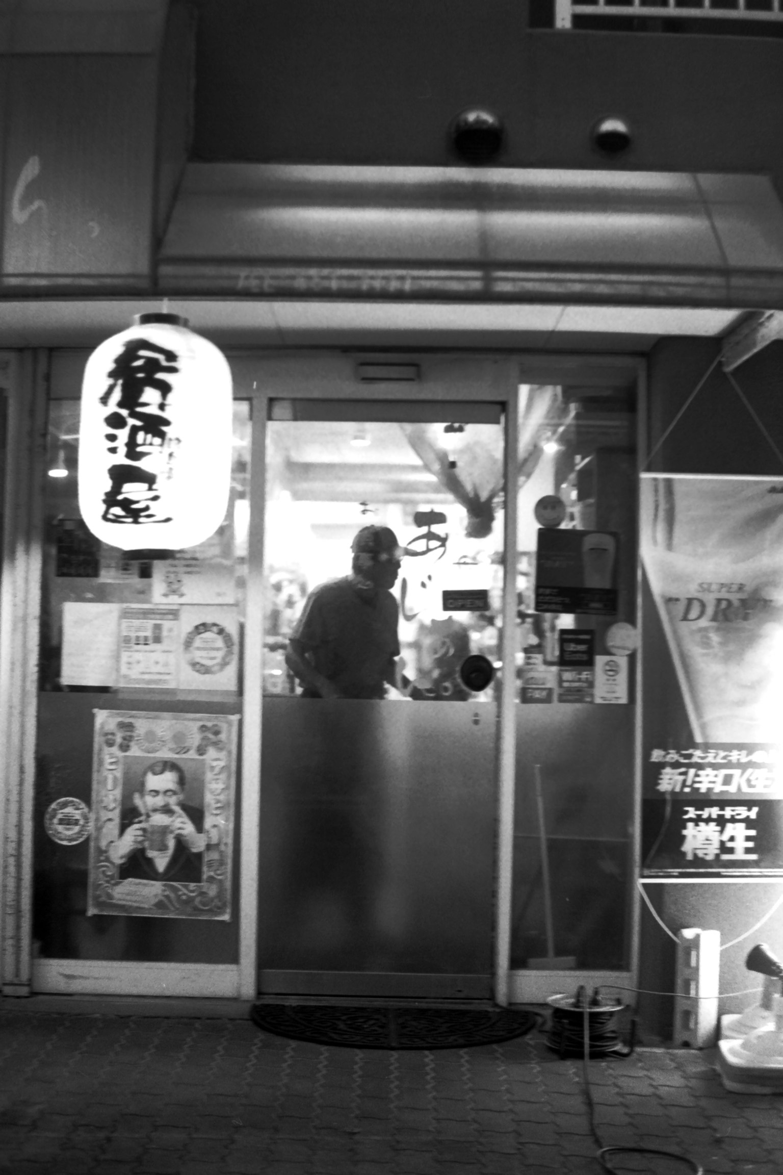 一个人在夜间商店的入口处站着，旁边有一个灯笼