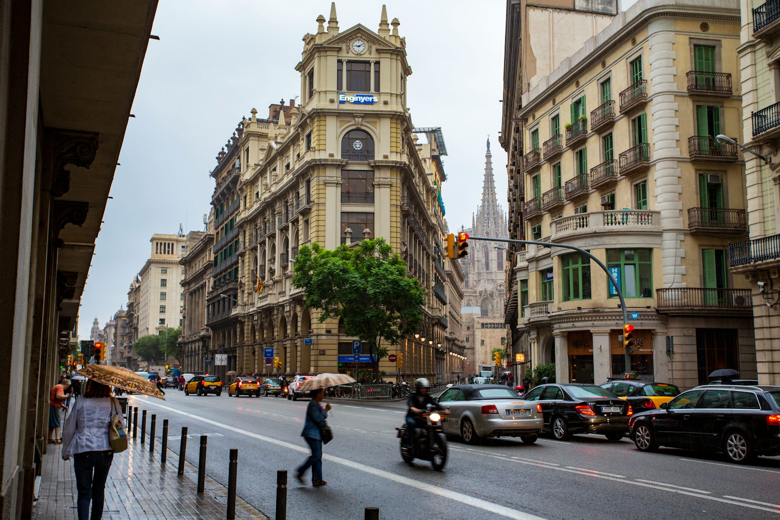 Straßenszene in Barcelona mit Fußgängern und Motorrädern im Regen