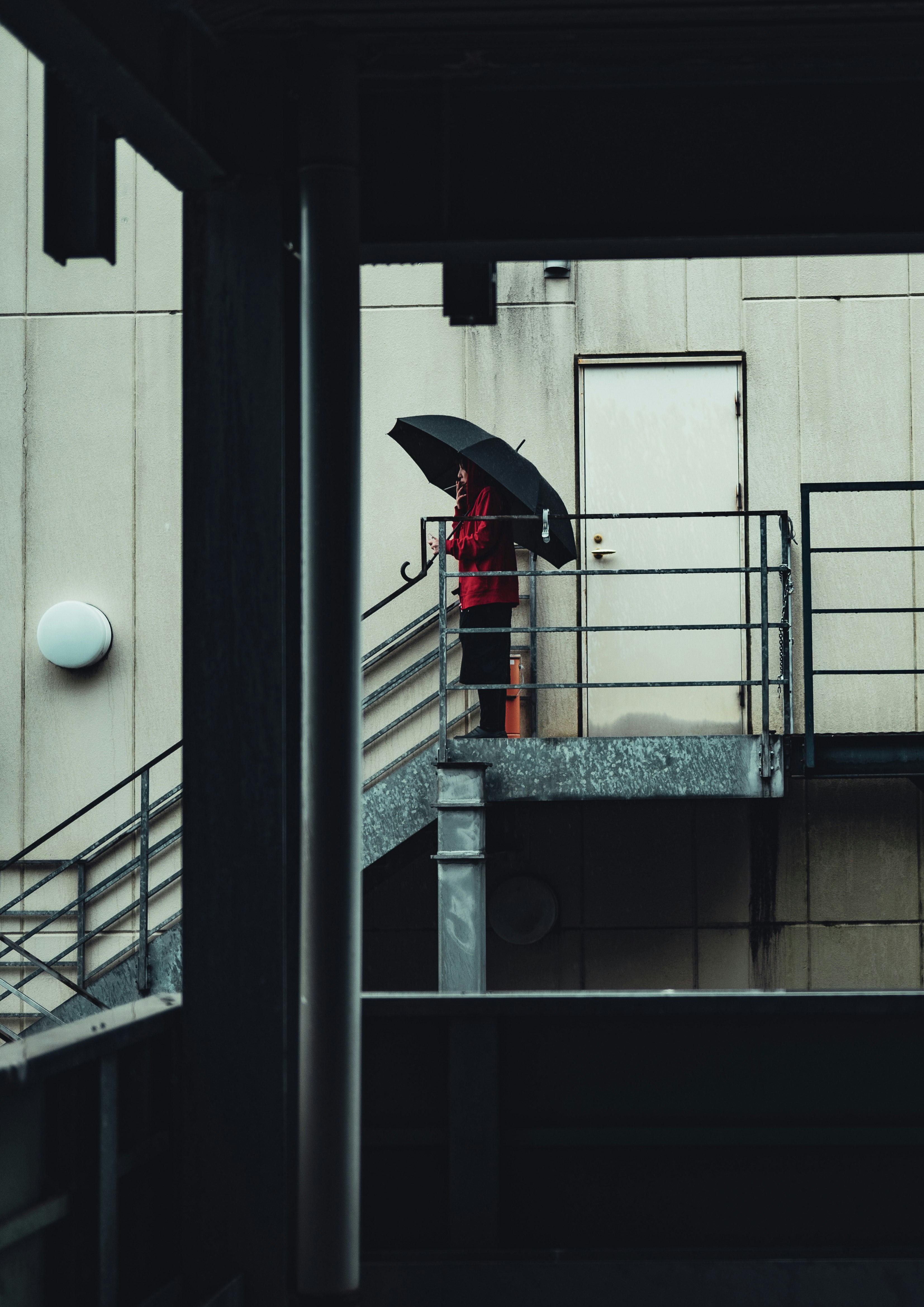 雨の路地で傘をさす人物が建物の通路に立つ