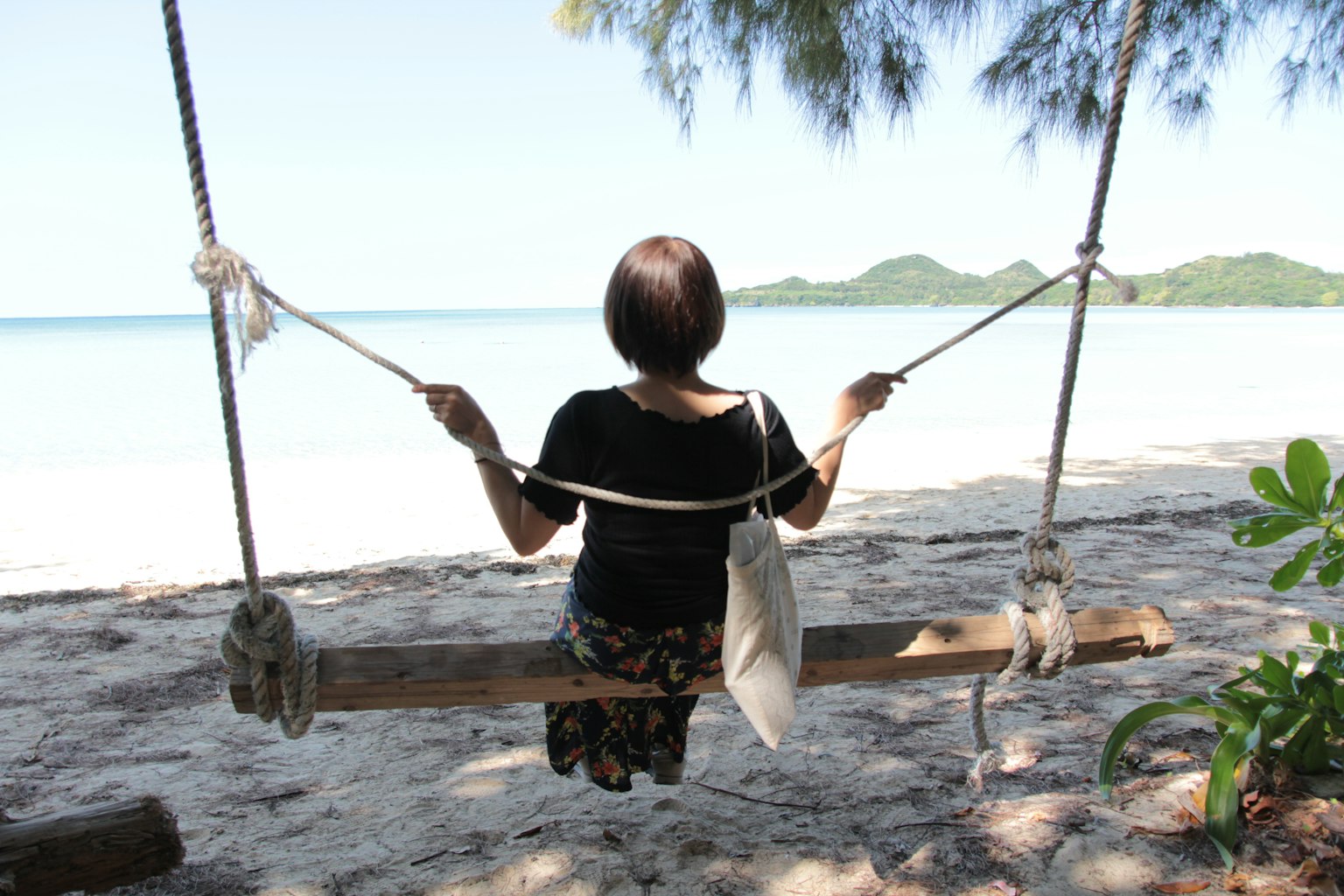 Wanita duduk di ayunan di pantai dengan pemandangan laut biru