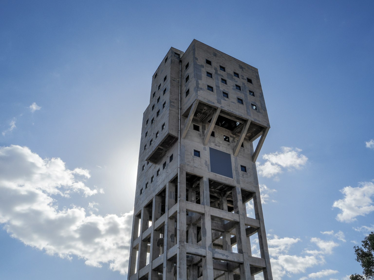 Sebuah menara beton tinggi berdiri di bawah langit biru menampilkan desain arsitektur unik