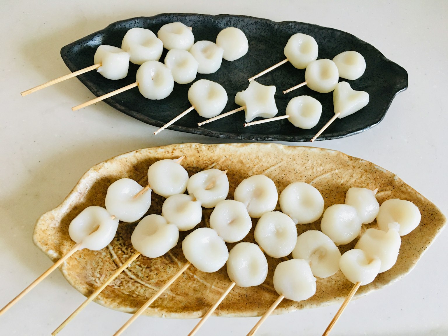Two plates with white dumplings on skewers arranged in different shapes